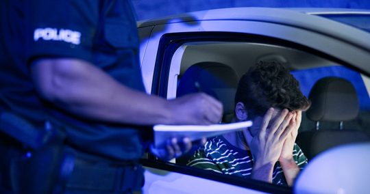 Officer writing a report while driver faces possible DUI arrest.